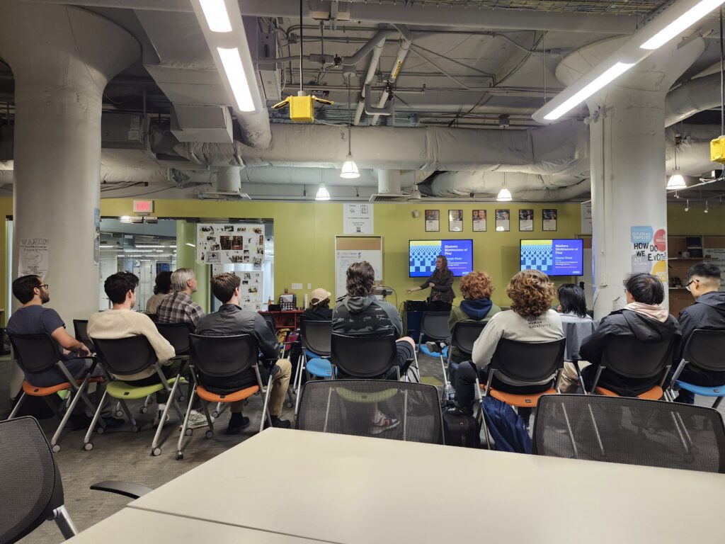 Author Cheryl Platz stands in front of a slide from her book The Game Development Strategy Guide while giving a guest lecture at Drexel University's Entrepreneurial Game Studio on November 5, 2025. A number of students and instructors are seen in the foreground.